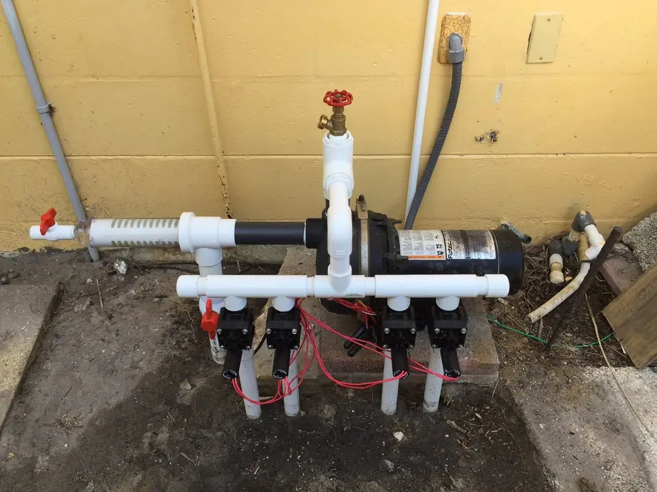A Hartmann pumping station: Flotec pump, brass shutoff, inline strainer and a four zone valve manifold mounted against a stucco wall